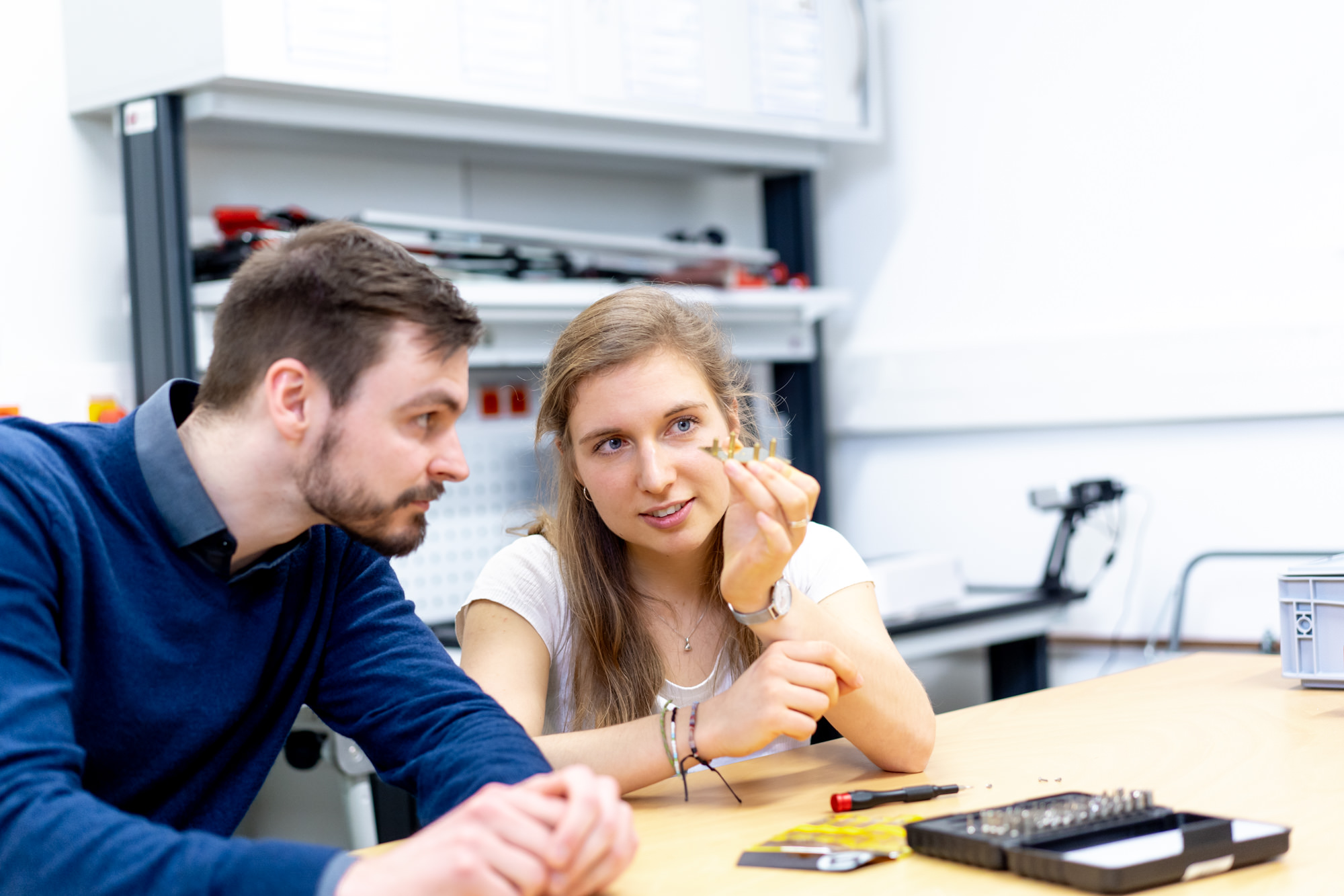 ein junger Mann und eine junge Frau sitzen an einem Tisch und schauen sich ein kleines Bauteil an